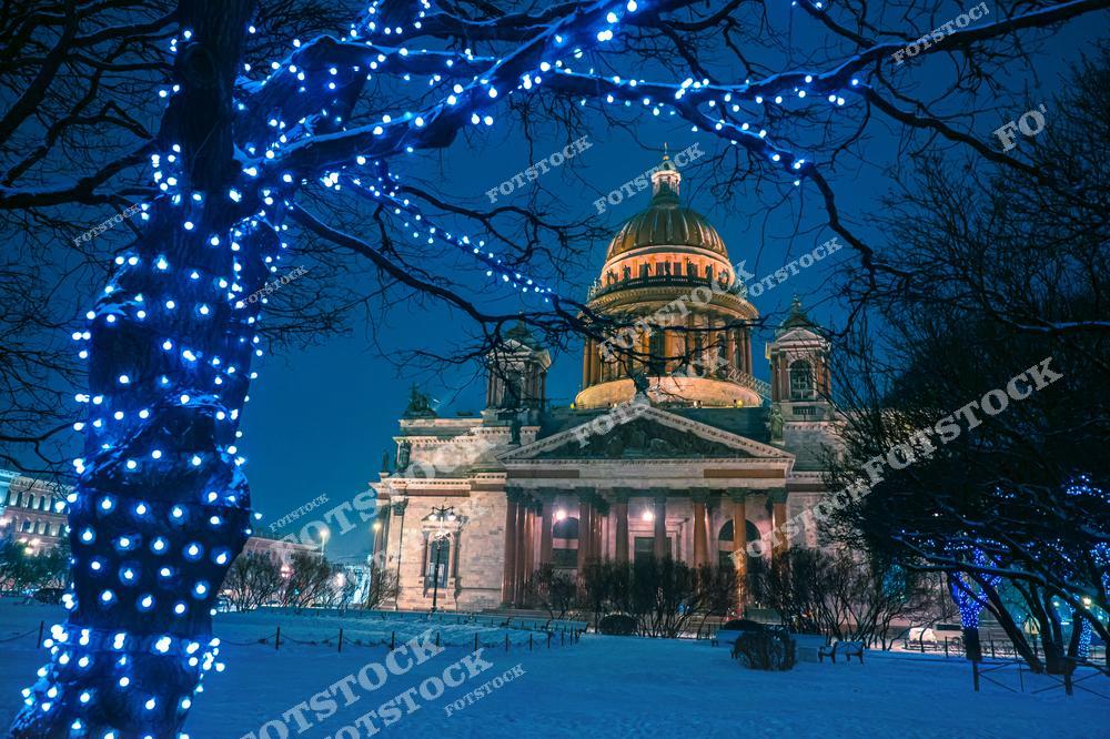 Фотография праздничного зимнего Санкт-Петербург, Россия, сделанная в период новогодних торжеств. На изображении запечатлён Исаакиевский собор, окружённый украшенными деревьями с сияющими световыми гирляндами. Этот фотоснимок передаёт атмосферу праздничного вечера: тёплый свет иллюминации, зимний пейзаж и торжественное настроение Нового года в России. Фото подчёркивает привлекательность зимнего путешествия в Петербург и его сказочный облик в праздничные дни. Иллюстрация может использоваться как картинка или слайд, посвящённые новогодним праздникам и зимнему туризму в Российской Федерации.